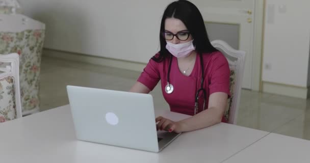 Медсестра в захисній масці з фонендоскопом на шиї, що друкується на клавіатурі — стокове відео