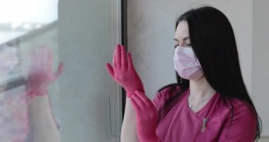 Responsible nurse corrects gloves before work and looking through the window