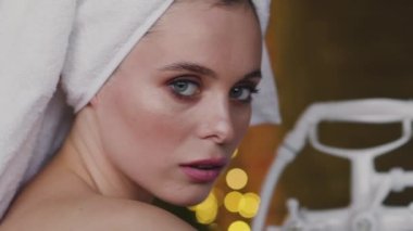 Kafasında havlu olan güzel bayan odadaki ışıklarla kameraya bakıyor.