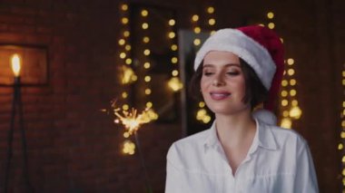 Noel Baba şapkalı ve gömlekli oyuncu kadın maytaplarla kamera karşısında eğleniyor.