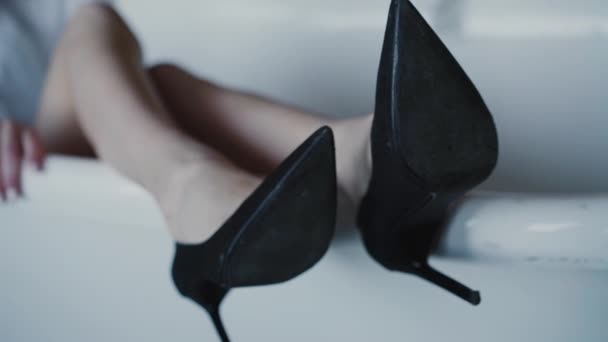 Kobieta w koszuli i butach na wysokich obcasach leżąca w wannie i przecinająca nogi — Wideo stockowe