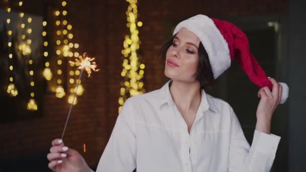 Mujer bonita en Santa Claus sombrero posando en la cámara con bengalas — Vídeos de Stock