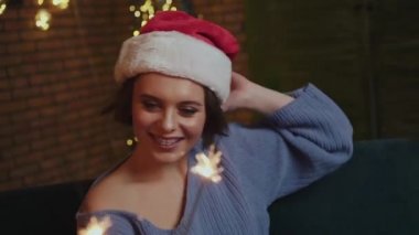 Noel Baba şapkalı gülümseyen kız yeni yıl havai fişekleriyle oynuyor.