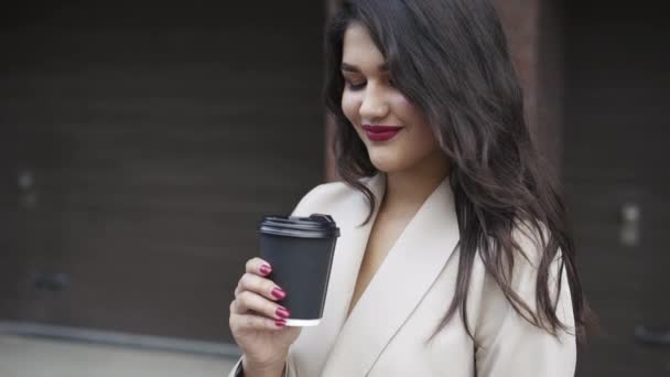 Mooie brunette met blazend haar en claret lippen bewondert een kopje drank — Stockvideo