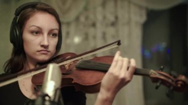 Kulaklıklı kadın müzisyen kemanla enstrümantal melodiyi prova ediyor.