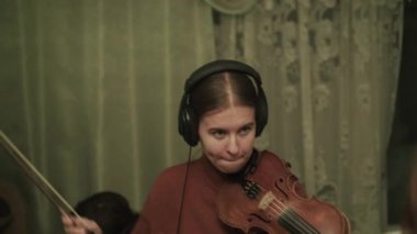 Kadın kemanla melodiyi prova ediyor hocasının akıl hocalığı altında kulaklık kullanıyor.