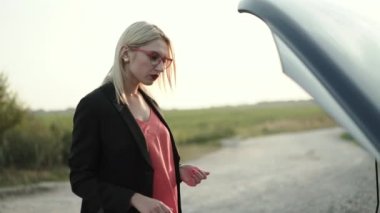 Sinirli sarışın gelir ve şehrin dışındaki bozuk bir arabanın kaputunun altına bakar.