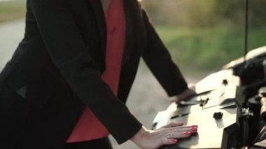 Şaşkın sarışın gün batımında şehir dışında bozuk bir arabanın kaputunun altına bakıyor.