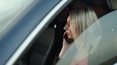 Gözlüklü sarışın arabaların ön koltuğunda telefonla konuşuyor.