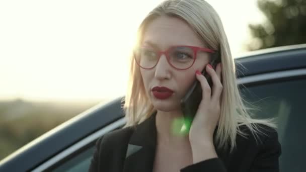 Блондинка разговаривает по телефону эмоционально в машине на шоссе на закате — стоковое видео