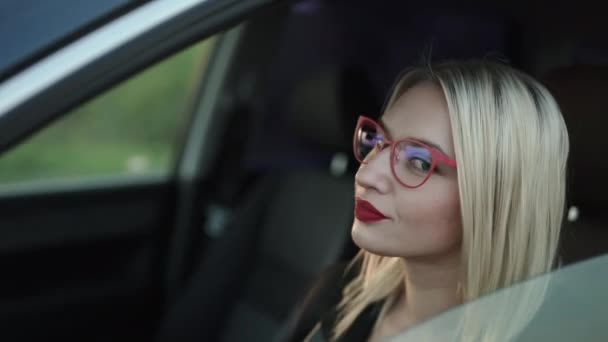 Hermosa dama con labios rojos sentada en el coche, gira y sonríe ante la cámara — Vídeos de Stock