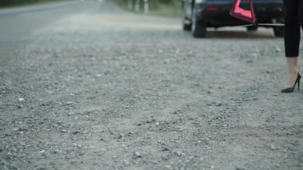 Femme méconnaissable avec une automobile cassée installant signe triangle rouge sur la route — Video