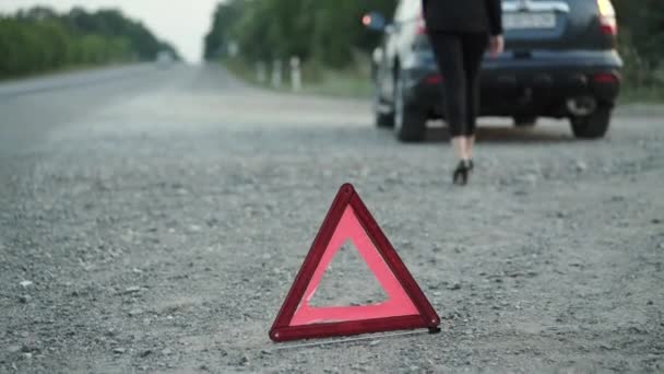 Donna irriconoscibile si appoggia su un'automobile rotta vicino al segno del triangolo rosso installato — Video Stock