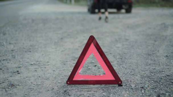 Onherkenbaar londe komt en leunt op gebroken auto in de buurt geïnstalleerde driehoek teken — Stockvideo