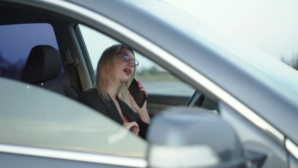Щаслива блондинка розмовляє з посмішкою на смартфоні, коли розслабляється в машині — стокове відео