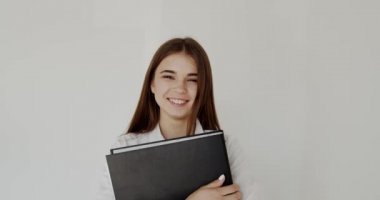 Elinde klasör olan ofis kızı beyaz arka plandaki kameraya bakıp gülümsüyor.