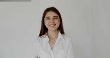 Çapraz elli neşeli genç kız, arka planda gülümsemeyle kameraya bakıyor.