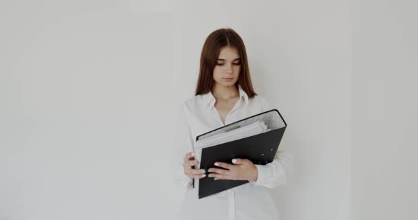 Szczęśliwa dziewczyna z czarnym folderem w rękach pozuje z uśmiechem na aparacie w biurze — Wideo stockowe