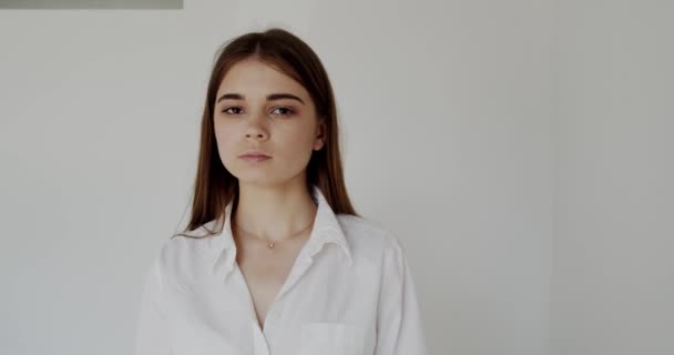 Retrato de una joven mirando a la cámara y cruzando las manos sobre fondo blanco — Vídeos de Stock