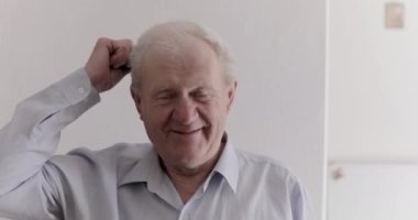 Neşeli son sınıf öğrencisi gri saçlarını tarıyor ve arka plandaki kameraya gülüyor.