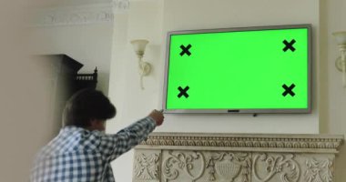 TV plazması izlerken adam uzaktan kumandayla kanalları değiştiriyor