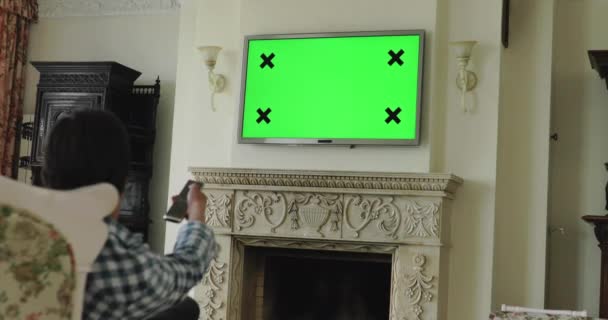 Мужчина отдыхает на диване, переключает каналы с удаленным от зеленого экрана телевизором с жестом — стоковое видео