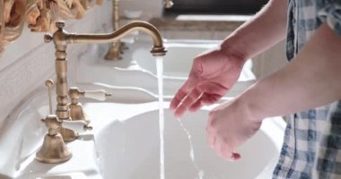 Adam musluğu açıyor, ellerini sabunluyor, tuvalette suyun altında yıkıyor.