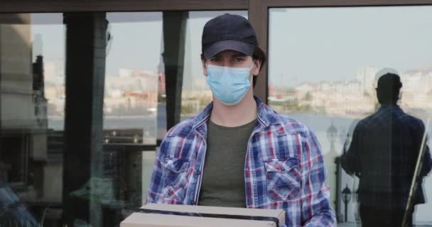 Retrato del hombre en máscara y guantes muestra un paquete en caja de cartón en la cámara — Vídeo de stock