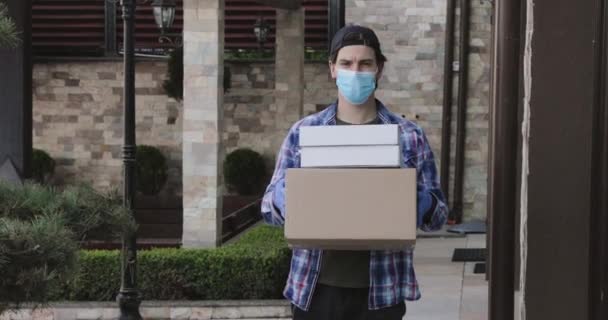 Junger Mann mit Maske und Handschuhen blickt selbstbewusst in die Kamera und zeigt Pakete — Stockvideo