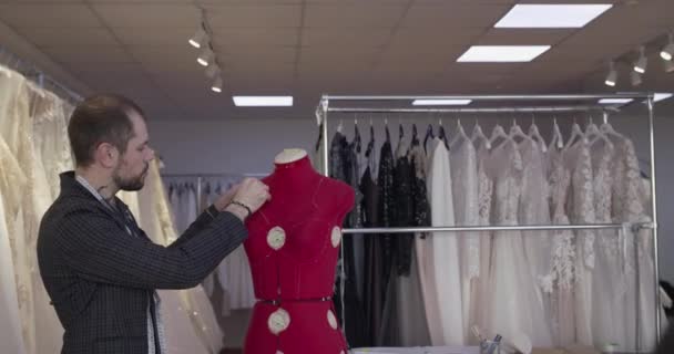 Guapo diseñador de bodas dibuja líneas punteadas en el maniquí de sastre deslizante en atelier — Vídeo de stock