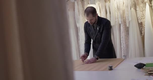 Ο ράφτης σχεδιάζει μια καμπύλη στον ιστό σε μια επιφάνεια εργασίας στο ατελιέ φόρεμα — Αρχείο Βίντεο