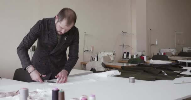 Der Modeschöpfer schneidet eine Stoffkurve auf einem Schreibtisch im Kleideratelier — Stockvideo