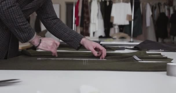 Krawiec rysuje oznaczenia na tkaninie z kredą na pulpicie w pracowni sukienki — Wideo stockowe