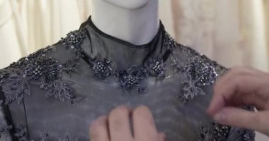 Terzinin elleri mankenin gece elbisesine iğneyi takar.