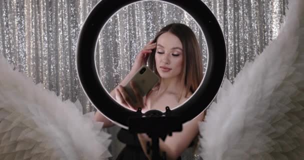 Mükemmel makyajlı çekici bir kız. Parlak arka planda güzel bir bayan manken yuvarlak lambanın içinden selfie çekiyor. — Stok video