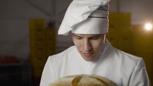 Baker em uniforme cheira um pão recém-assado, tem um prazer e parece — Vídeo de Stock