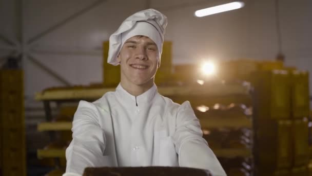 Um jovem padeiro com um sorriso apresenta pão de centeio para a câmera na padaria — Vídeo de Stock