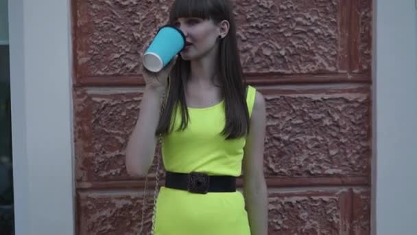 Junge Dame in hellgrünem Kleid mit Getränk in der Hand posiert am Gebäude — Stockvideo