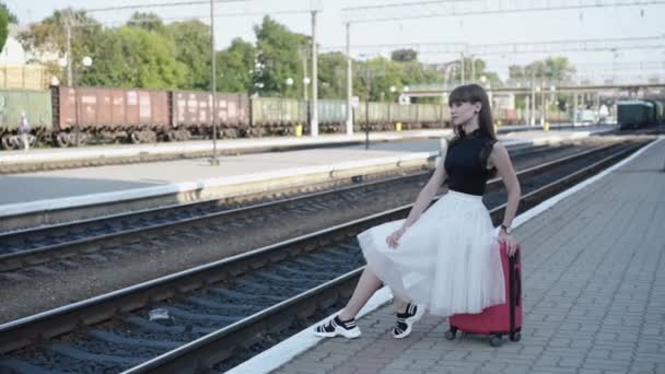 Senhora feliz em vestido preto-branco sentado em poses na mala na ferrovia — Vídeo de Stock