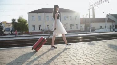 Elbiseli mutlu bayan valiziyle ve platformda dönüyor.