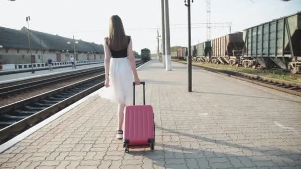 Hübsches Mädchen läuft mit Koffer auf Bahnsteig und winkt dem Zug zu — Stockvideo