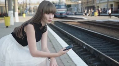 Düşünceli kız demiryolu platformunda telefon kullanıyor.