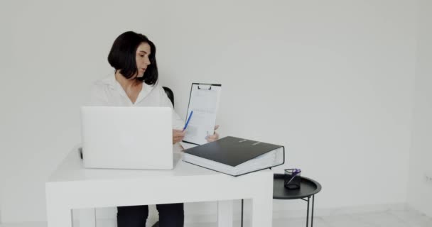 Γυναίκα δάσκαλος συνομιλίας στο φορητό υπολογιστή χρησιμοποιώντας σημειωματάριο στο γραφείο με λευκό εσωτερικό — Αρχείο Βίντεο