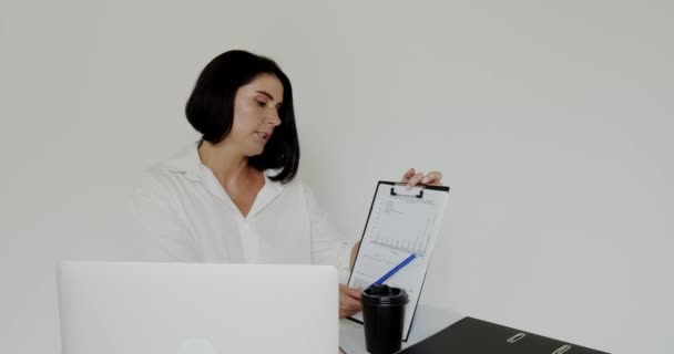 Dozent plaudert am Laptop mit Notizbuch, trinkt Kaffee im Büro — Stockvideo