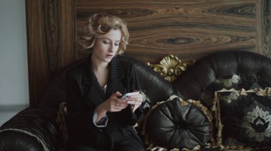 Lüks koltukta oturan, akıllı telefondan yazan ve yan odaya bakan bir kadın.