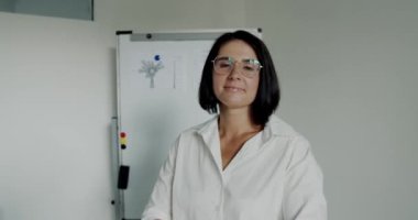 Kendine güvenen öğretmenin portresi gözlüğü düzeltir ve ofisteki kameraya gülümser.