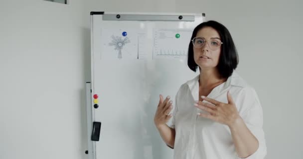 Referentin erklärt Thema mit Gesten vor Kamera am Whiteboard — Stockvideo
