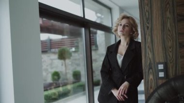 Siyah takım elbiseli güzel bir model duvara yaslanıyor ve ellerini çapraz yapıyor.