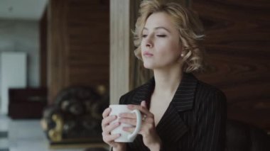 Penceredeki koltukta oturan düşünceli bayan, içiyor ve onu seyrediyor.