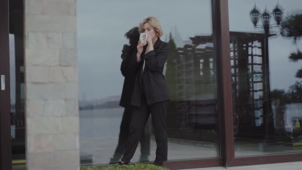 Krásná žena v černém obleku pije šálek nápoje a pózuje doma — Stock video